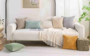 Home Decor Finds Under $50 featuring a cozy white sofa with textured neutral, green, and mustard pillows, a soft throw blanket, and modern living room decor.
